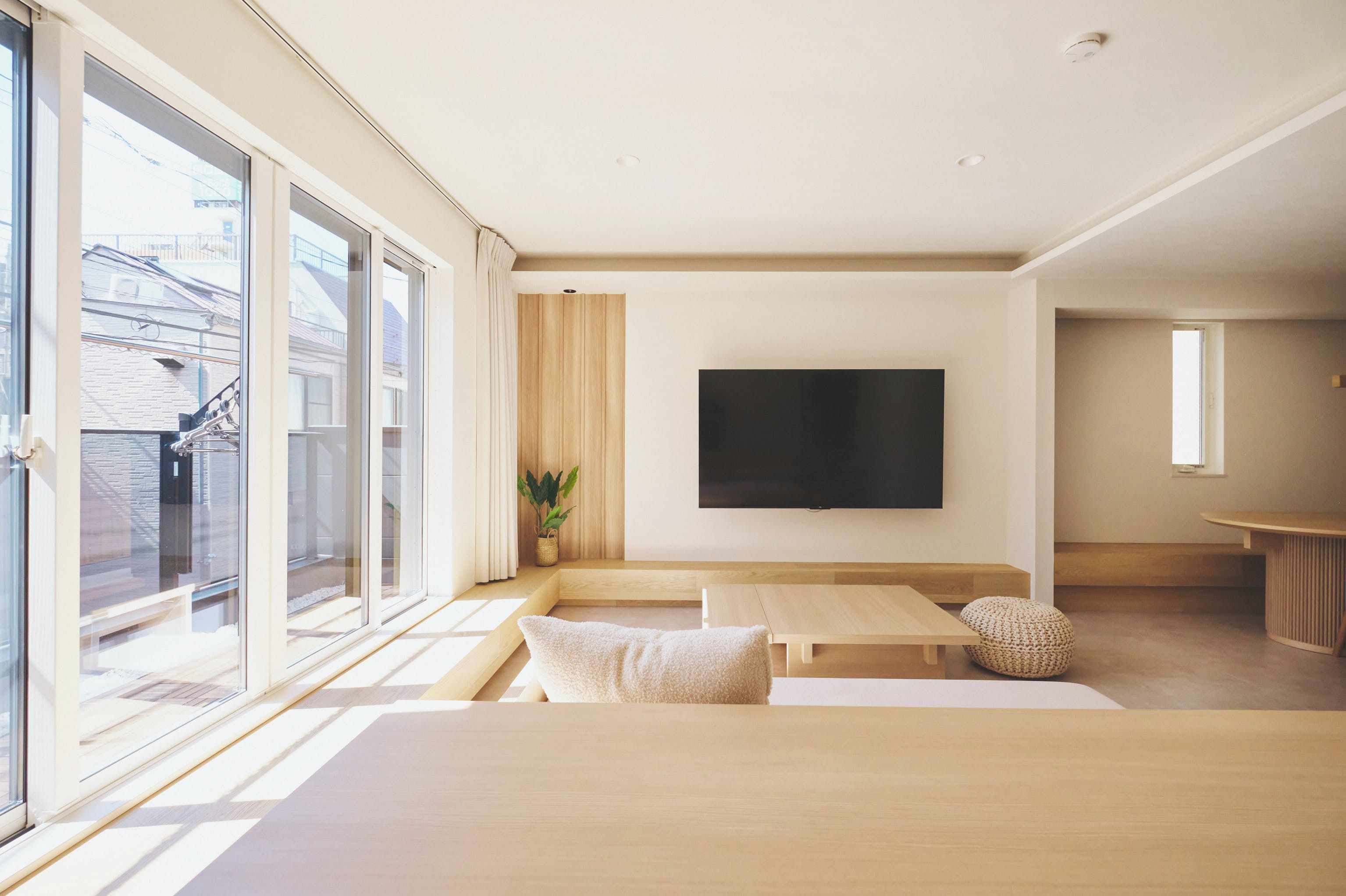 A modern living room with a large TV, wooden furniture, and a view of a building outside.