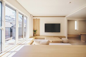 A modern living room with a large TV, wooden furniture, and a view of a building outside. - New Listing (新宿区中落合１丁目２１－３　中落合ホテル)