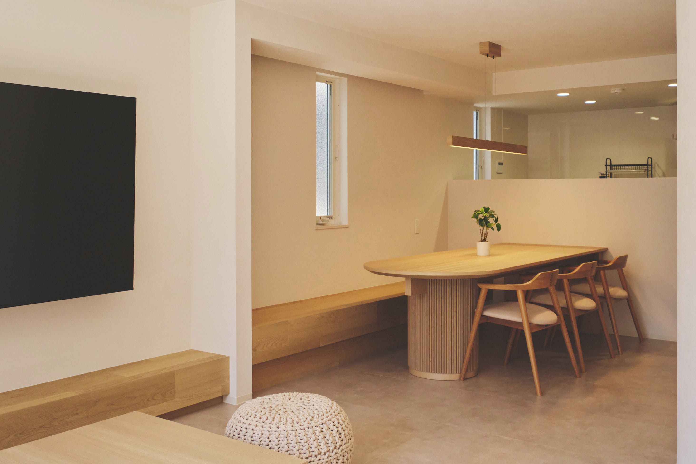 A modern dining area with a wooden table and chairs, a small potted plant, and a large flat-screen TV mounted on the wall.