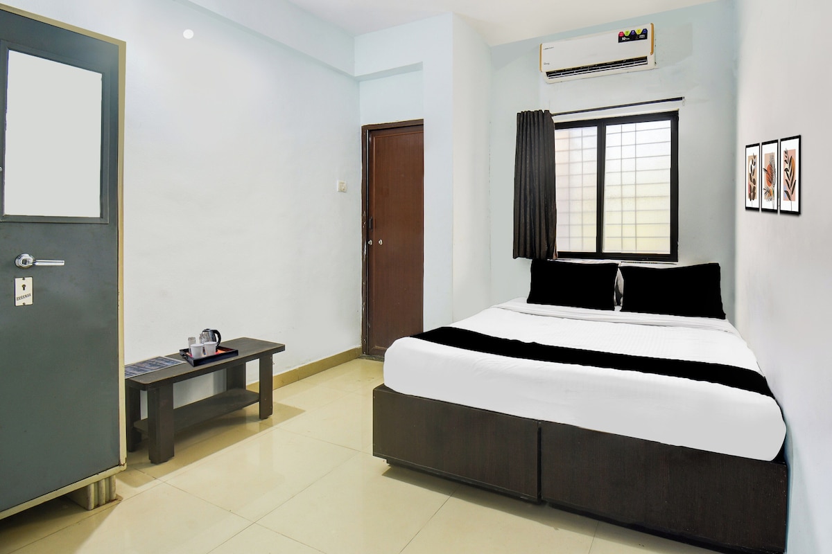 Quarto de hotel com cama, escrivaninha, cafeteira e janela com cortinas.