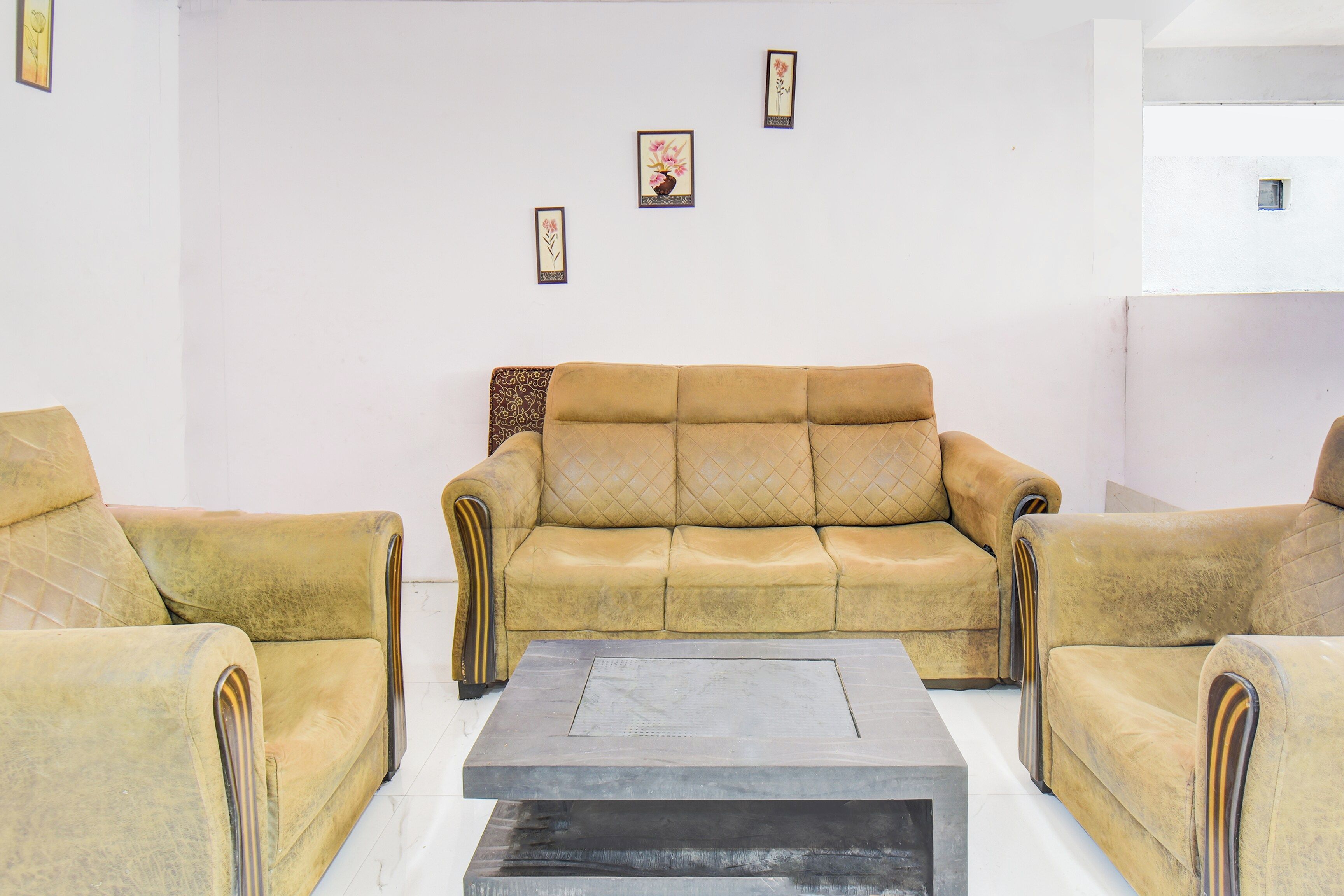 Una sala de estar con un sofá y dos sillones, una mesa de centro y tres cuadros en la pared.