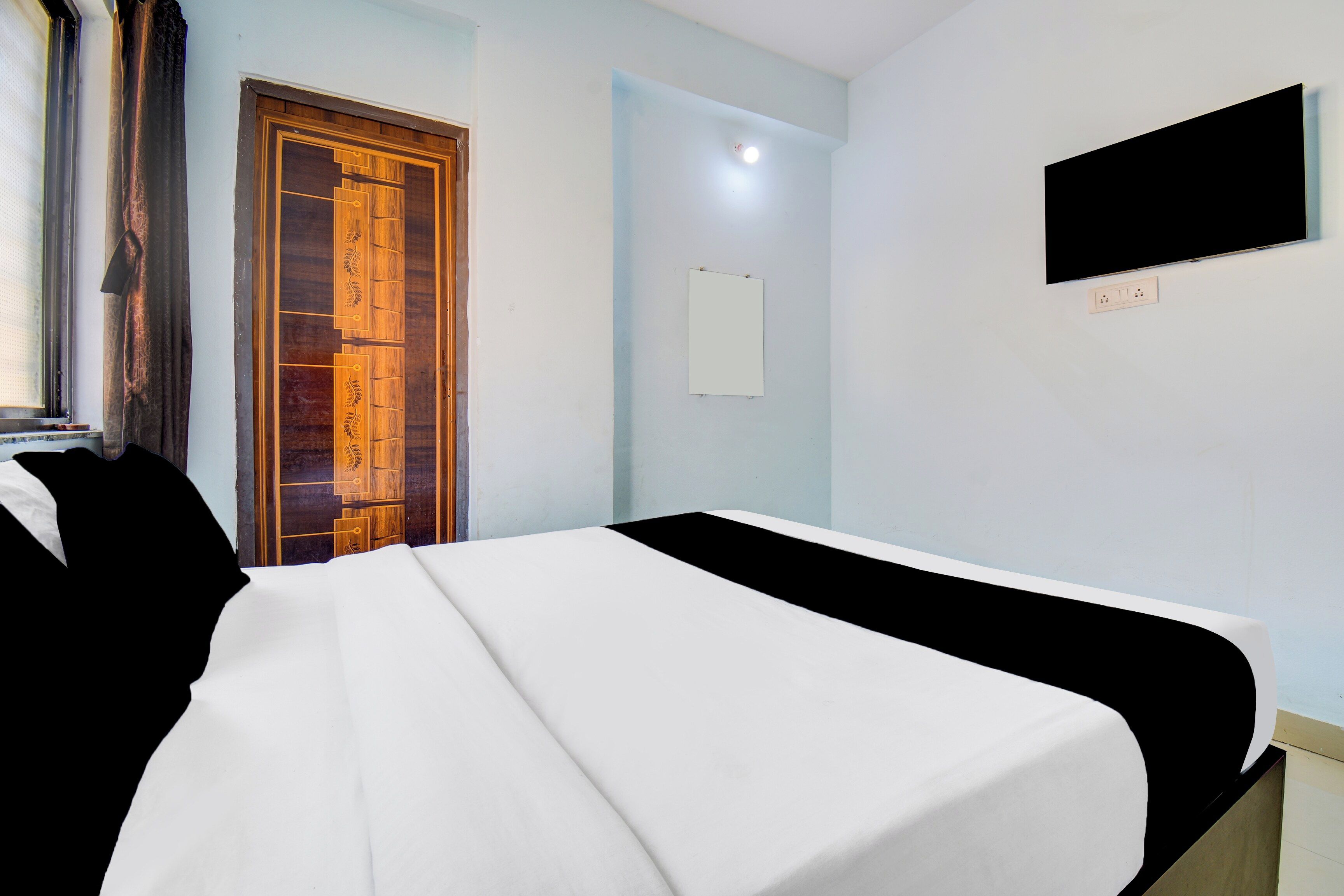 Une chambre d’hôtel avec un lit, une porte en bois, un téléviseur fixé au mur et un interrupteur.