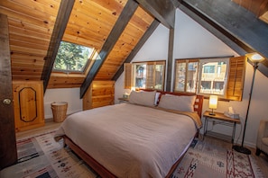 A bedroom with a large bed, wooden ceiling beams, a window, and a nightstand with a lamp. - Ludwig's Lodge: 5 Bedroom, 3 bathroom Dollar Point home. (Tahoe City)