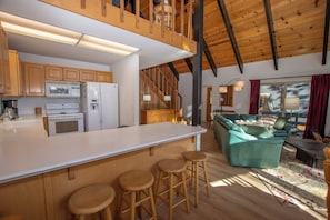 A modern kitchen with a central island, wooden bar stools, a dining area with a sofa and a coffee table, and a staircase leading to an upper level. - Ludwig's Lodge: 5 Bedroom, 3 bathroom Dollar Point home. (Tahoe City)