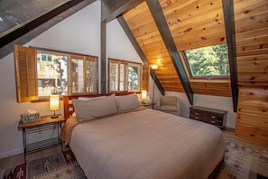 A bedroom with a large bed, wooden ceiling beams, and a window with shutters. - Ludwig's Lodge: 5 Bedroom, 3 bathroom Dollar Point home. (Tahoe City)