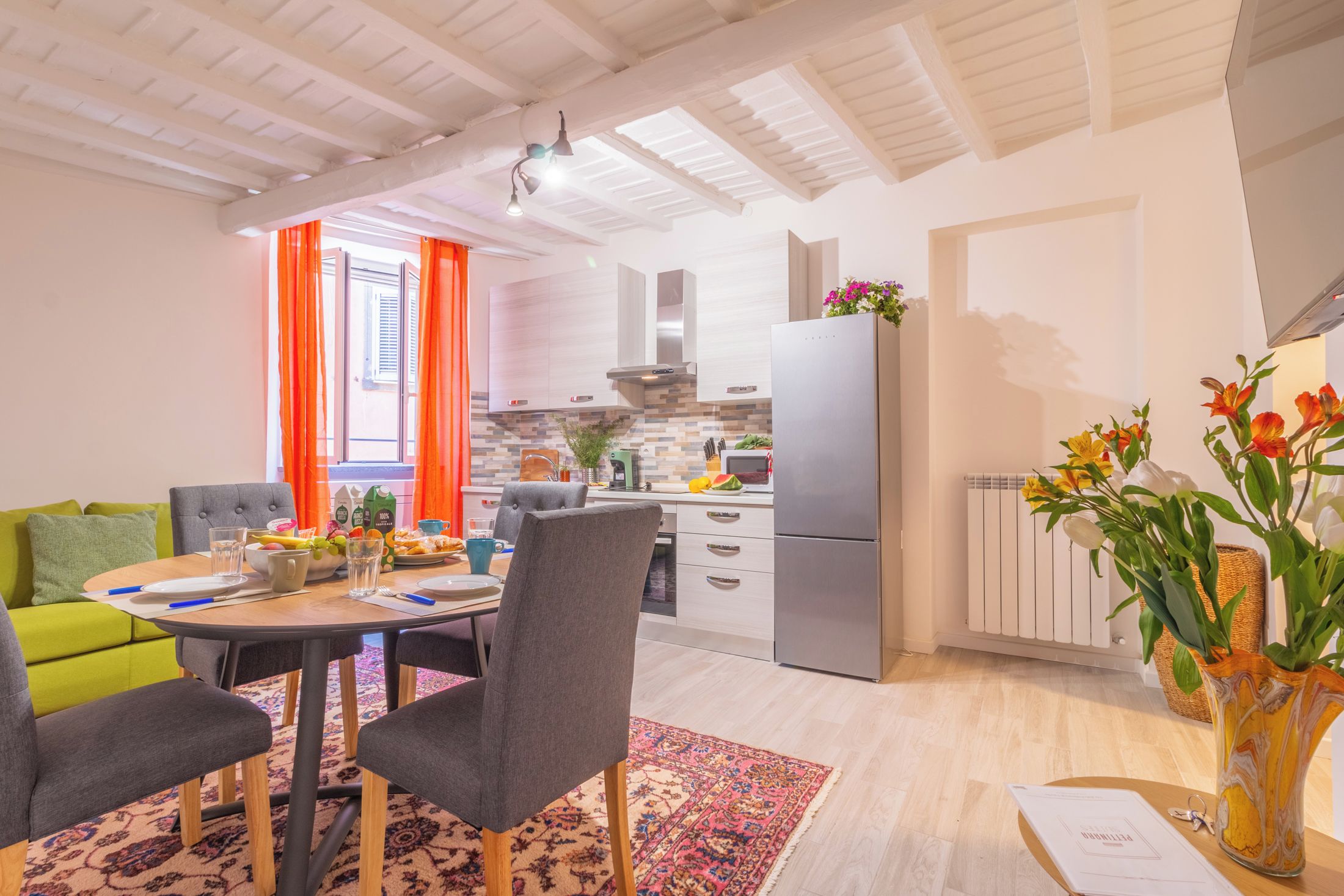 A modern kitchen with a refrigerator, stove, and cabinets. There is a dining area with a table and chairs, and a living room with a sofa.
