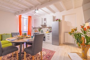 A modern kitchen with a refrigerator, stove, and cabinets. There is a dining area with a table and chairs, and a living room with a sofa. - Pettinara Suites (Viterbo)