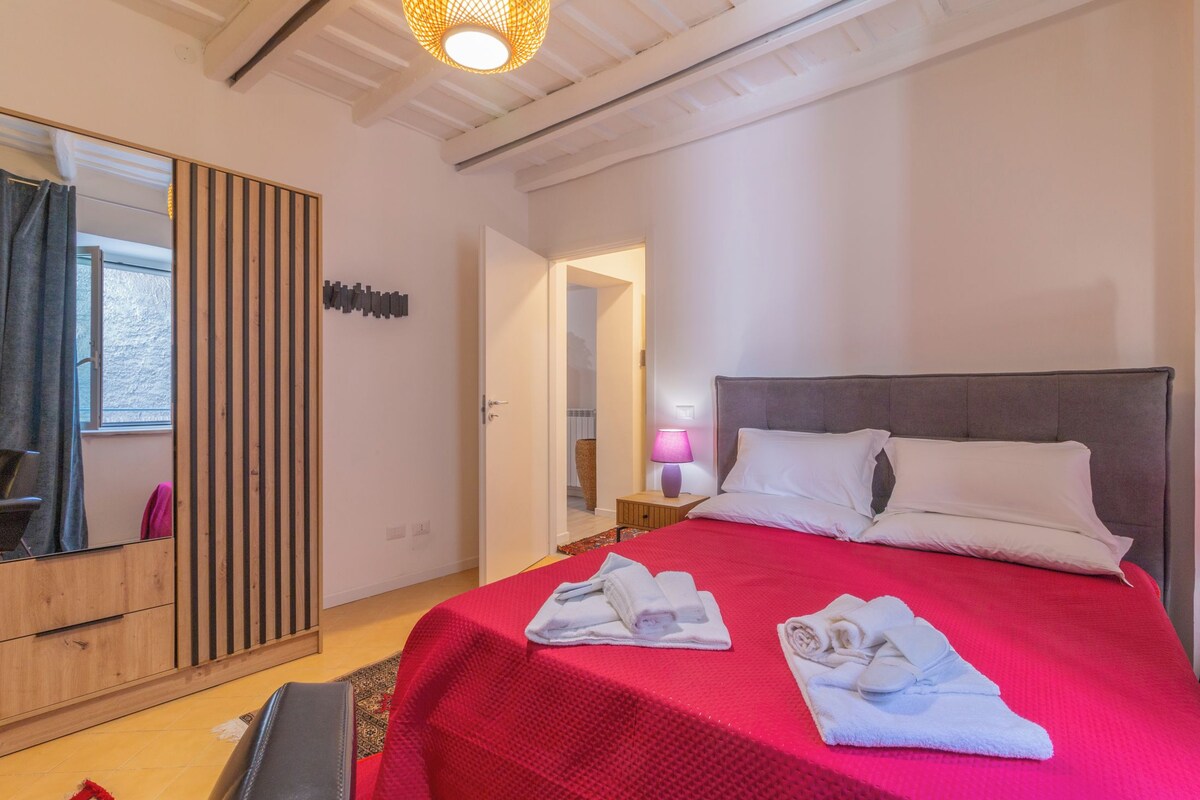 A hotel room with a large bed, a wooden wardrobe, a mirror, and a door leading to another room.