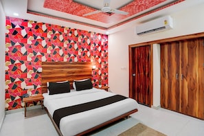 Un dormitorio con pared de estampado geométrico, cabecera de madera, cama con ropa blanca, mesita de noche y armario de madera. También se observa un aire acondicionado instalado en la pared.
