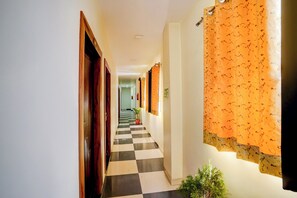 Un pasillo con piso ajedrezado, puertas de madera y cortinas con estampado naranja.