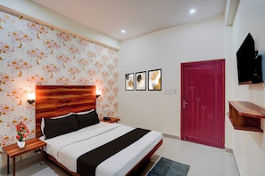 Habitación de hotel con una cama, mesitas de noche, una puerta roja, televisor montado en la pared y un diseño de papel tapiz con motivos florales.