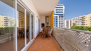 A balcony with a dining area, sliding glass doors, and a view of adjacent buildings. - 2BR Flat with Balcony & Shared Pool by LovelyStay (Portimão)