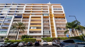 A multi-story residential building with balconies, a central stairwell, and a parking area with cars. - 2BR Flat with Balcony & Shared Pool by LovelyStay (Portimão)
