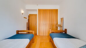 A room with two single beds, a wooden wardrobe, a wall-mounted lamp, and a door. - 2BR Flat with Balcony & Shared Pool by LovelyStay (Portimão)