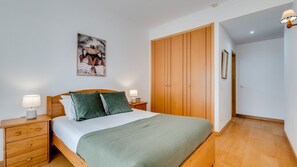 A bedroom with a bed, wooden wardrobe, nightstands, and a wall-mounted picture. - 2BR Flat with Balcony & Shared Pool by LovelyStay (Portimão)