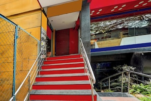 A staircase with red steps leading to a closed door, surrounded by a yellow wall and a chain-link fence. - Super Hotel O Mathikere Extension (Bangalore)