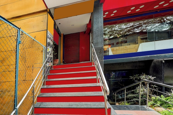 A staircase with red steps leading to a closed door, surrounded by a yellow wall and a chain-link fence.
