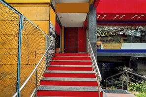 A staircase with red steps leading to a closed door, surrounded by a yellow wall and a chain-link fence. - Super Hotel O Mathikere Extension (Bangalore)