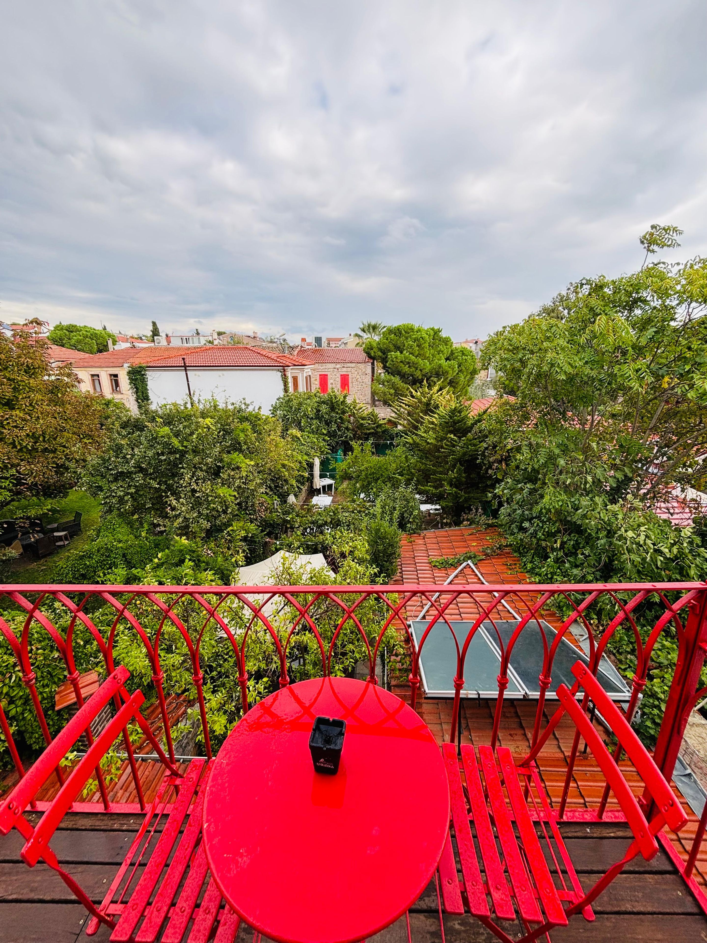 A red table and chairs on a balcony overlooking a courtyard with trees and buildings.