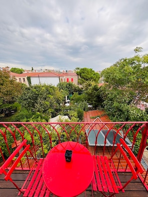 Una mesa y sillas rojas en un balcón con vistas a un patio con árboles y edificios.