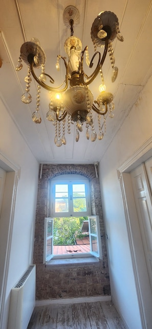 Una habitación con candelabro, ventana con vista a follaje y pared de piedra.