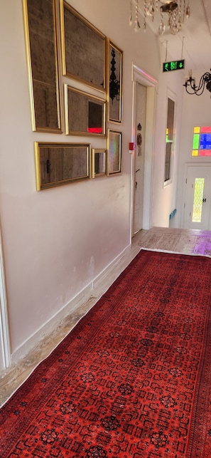 Un pasillo con alfombra roja estampada, una pared con varios espejos enmarcados y una puerta con letrero de salida.