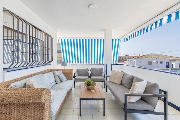 A balcony with a wicker sofa, a grey sofa, and two armchairs. There is a wooden table with a plant.