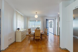 A dining area with a round table, six chairs, a white cabinet, and a window with curtains.