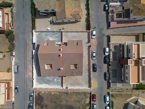 An aerial view of a parking lot with multiple cars, a building with a sloped roof, and a fenced area.