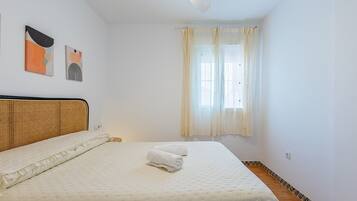 A bedroom with a bed, a headboard, a window with curtains, and two wall art pieces.