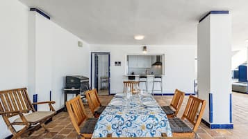 A dining area with a long table, chairs, a grill, and a kitchen area with cabinets and a sink.
