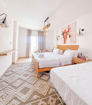 Ett hotellrum med en stor säng, en mindre säng, ett nattduksbord, en stol, ett fönster med gardiner och en tavla på väggen.