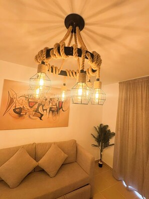 A room with a beige sofa, a painting on the wall, a potted plant, and a curtain. - Edelma Retreat 2BR Pool Views, Sahl Hasheesh (Red Sea Governorate)