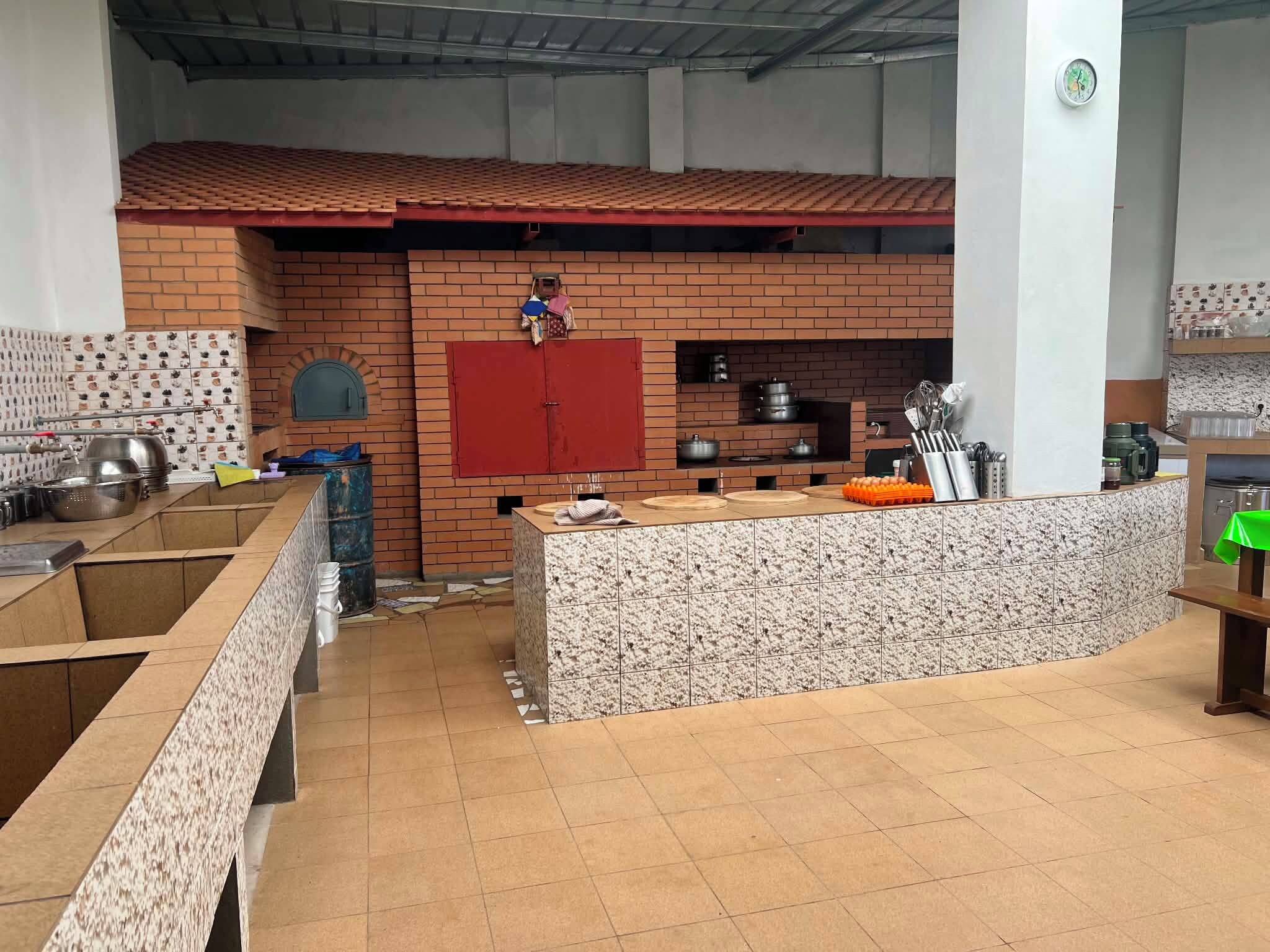 A kitchen with a brick wall, a red cupboard, and various cooking utensils.