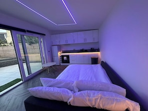 A modern bedroom with a large bed, a sliding glass door to the outside, and a kitchenette area. - Amazing guest house for a romantic get away (Edinburgh)