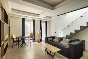 A modern living room with a sofa, a coffee table, and a dining area with chairs. There is a staircase leading to an upper floor. - Macsuites Central Market (Valencia)