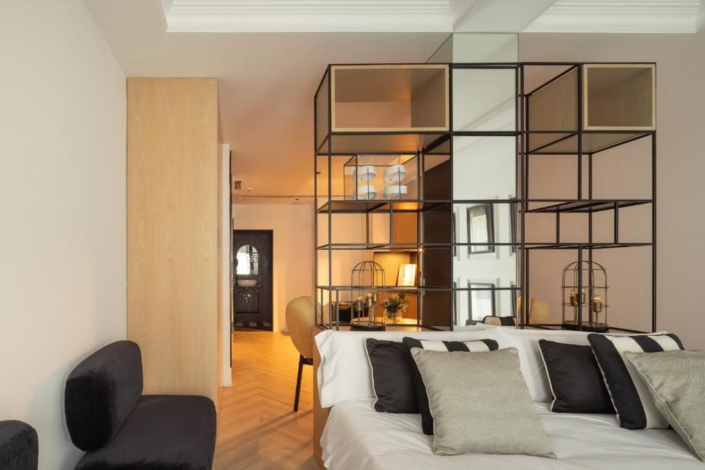 Una habitación de hotel moderna con una cama, un sillón negro, una puerta de madera y un aparador con espejo.