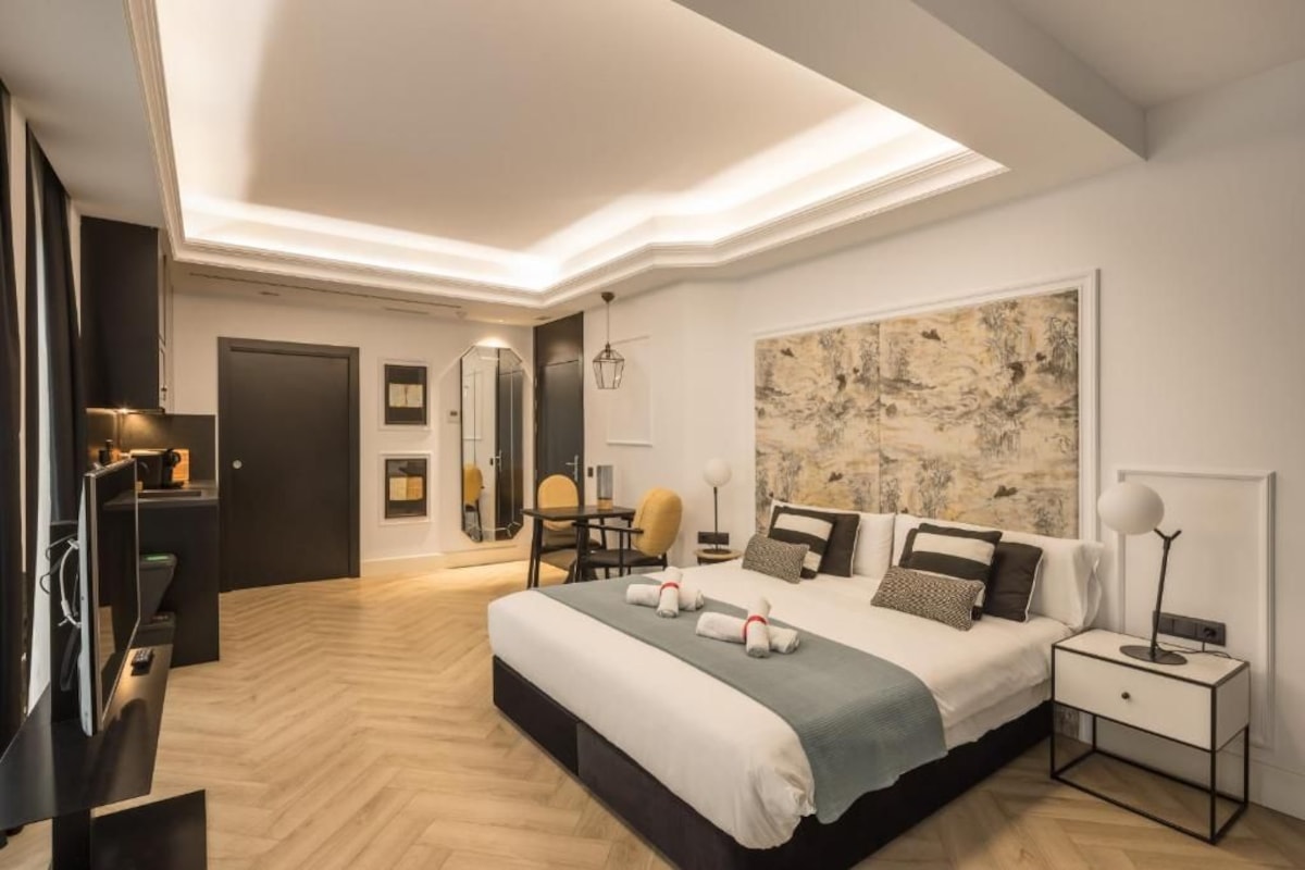 A modern hotel room with a large bed, a desk, a chair, and a large abstract painting on the wall.