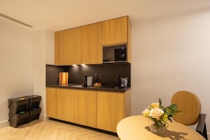 A modern kitchen with wooden cabinets, a black countertop, and a microwave. There is a small table with a vase of flowers. - Macsuites Central Market (Valencia)