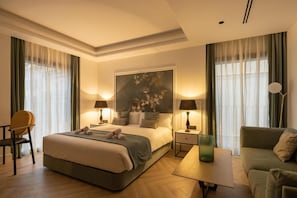 A hotel room with a bed, bedside tables, a chair, a sofa, and a painting on the wall. - Macsuites Central Market (Valencia)