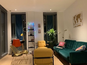 Ein modernes Wohnzimmer mit einem grünen Sofa, gelben Sesseln und einem roten Sessel. Es gibt eine Pflanze, einen Globus an der Wand und einen Schreibtisch mit einer Lampe.