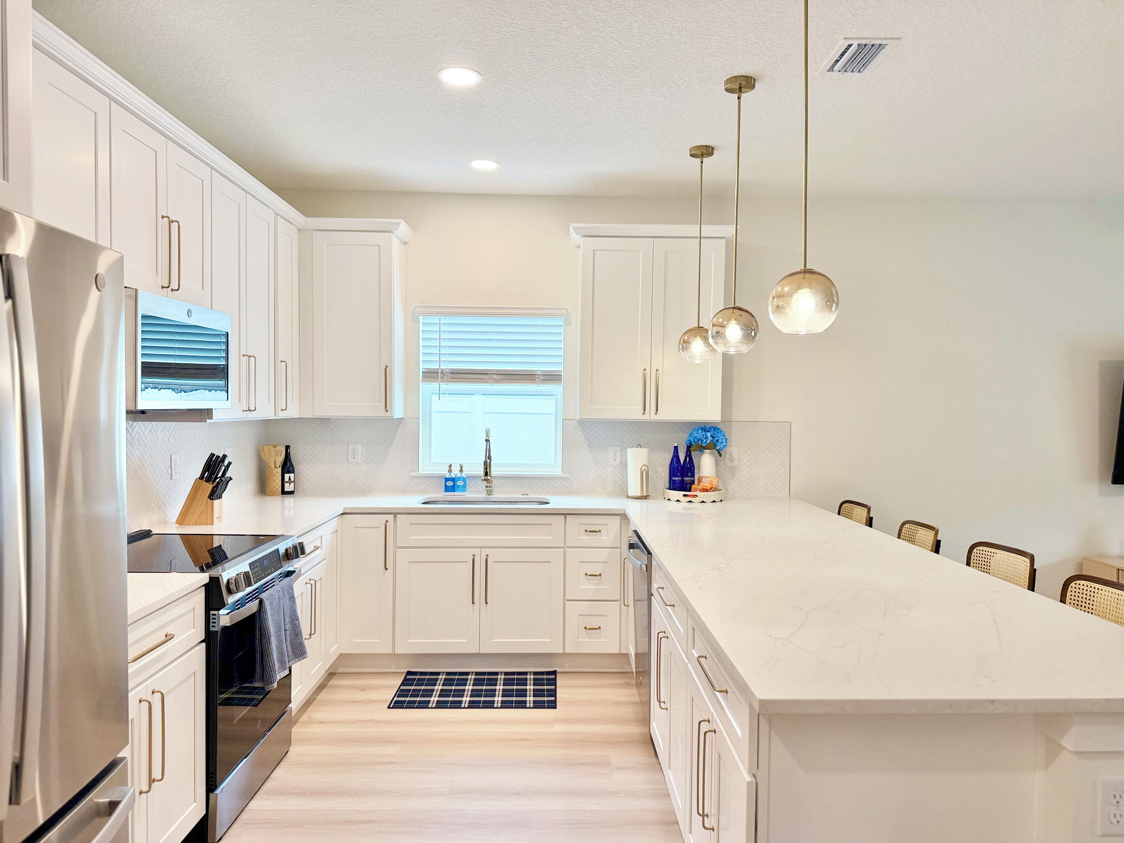 A modern kitchen with white cabinetry, stainless steel appliances, and pendant lighting.