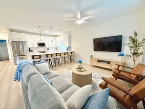 A modern living room with a sofa, coffee table, and a TV mounted on the wall. - Azure & Anchor Coastal Escape W Huge Fenced Yard & Fire Pit + Small-Pet-Friendly (St. Augustine)