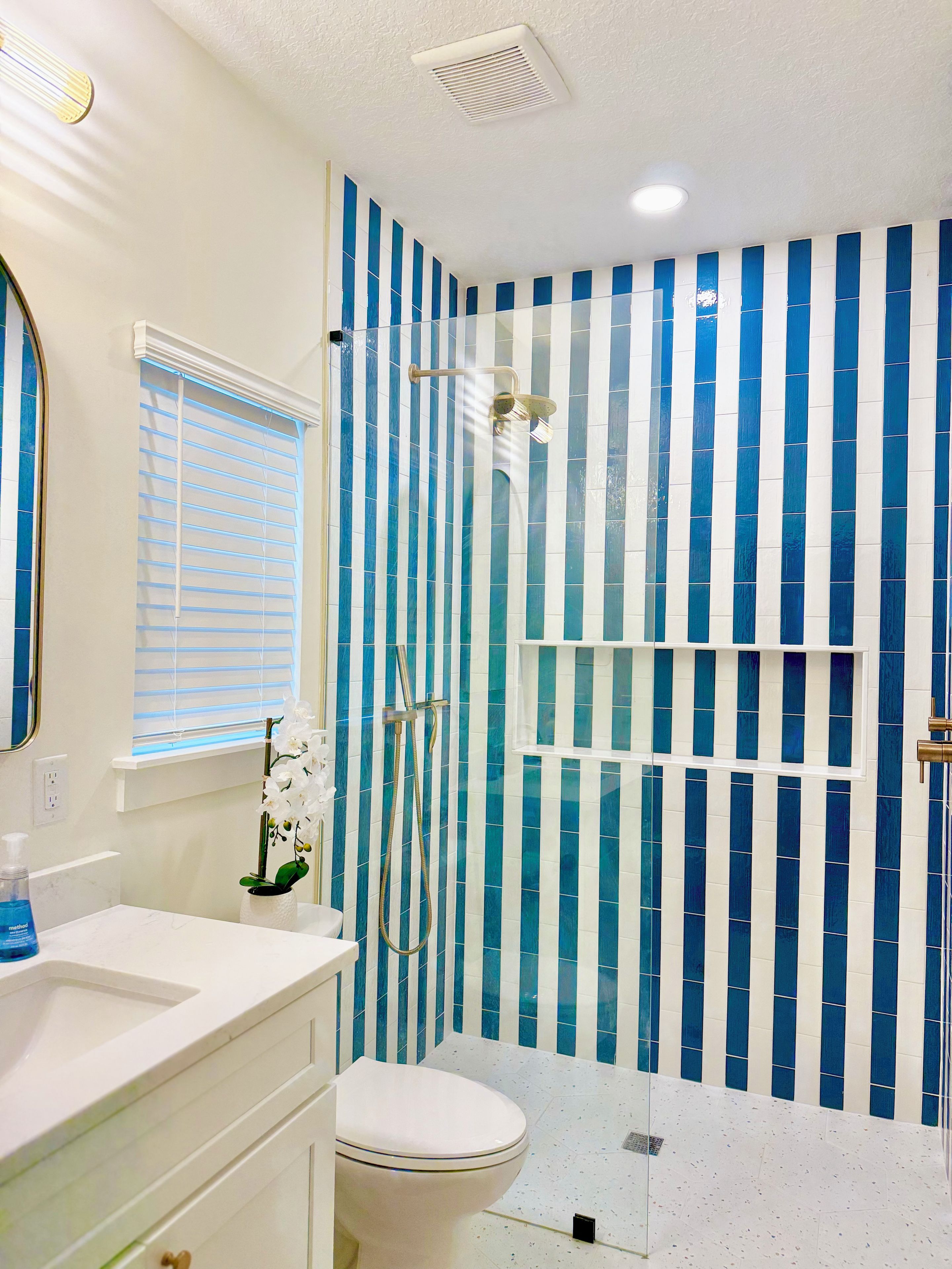 A bathroom with a white toilet, a sink, and a shower with blue-striped tiles.
