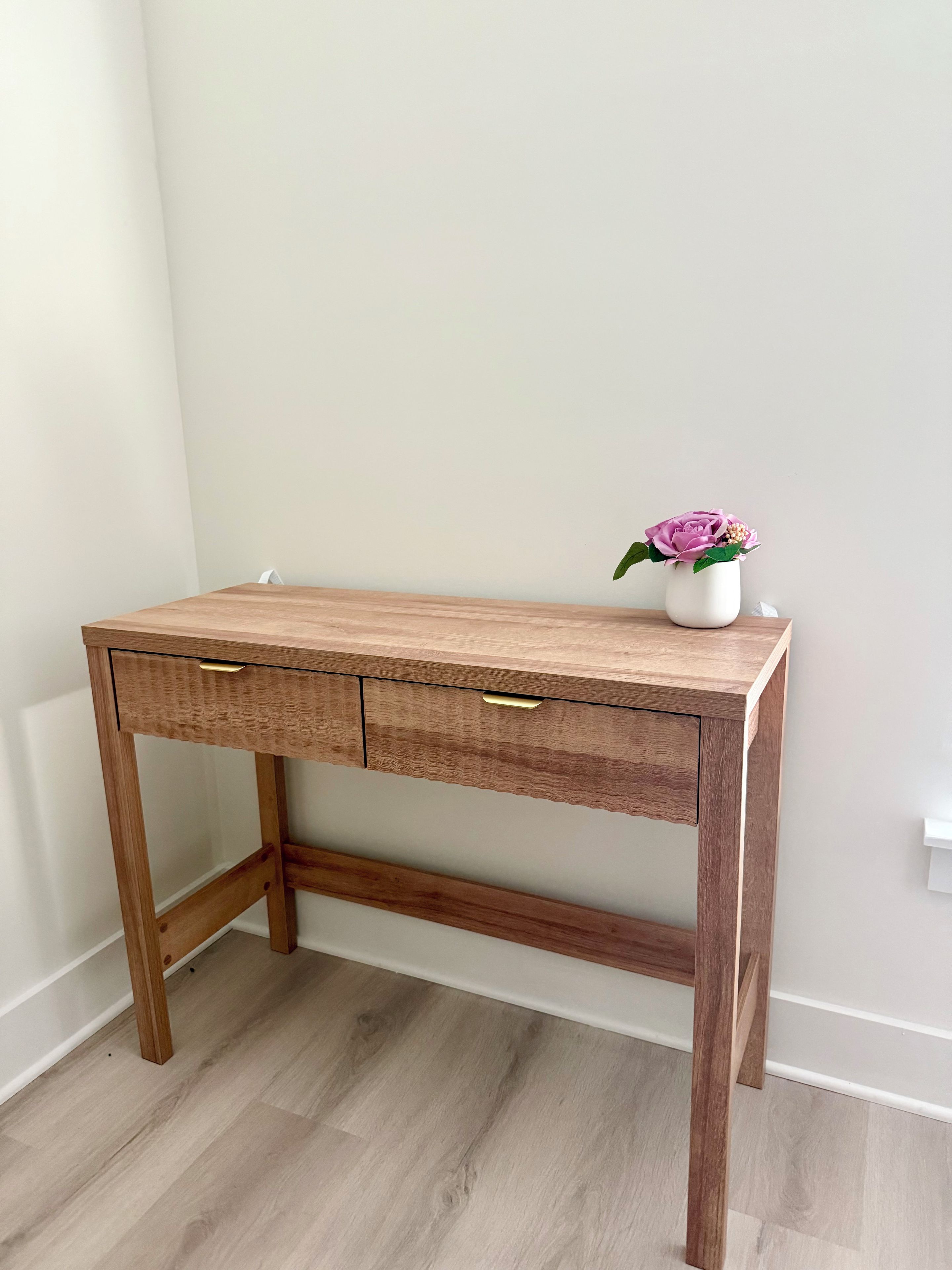 A wooden desk with two drawers and a vase with a flower on top.