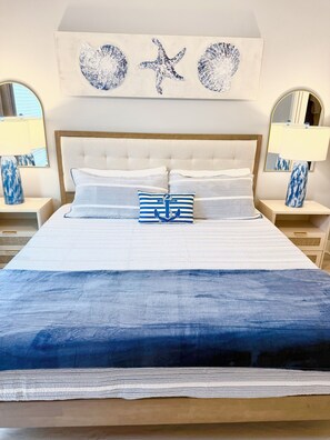 A bed with a striped pillow and a blue blanket, flanked by two nightstands with lamps. - Azure & Anchor Coastal Escape W Huge Fenced Yard & Fire Pit + Small-Pet-Friendly (St. Augustine)