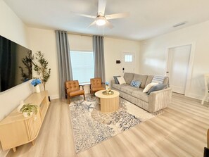 A modern living room with a sofa, two armchairs, a coffee table, and a TV. - Azure & Anchor Coastal Escape W Huge Fenced Yard & Fire Pit + Small-Pet-Friendly (St. Augustine)