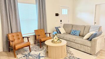 A living room with a beige sofa, two brown leather chairs, a round wooden coffee table, and a star-patterned rug.