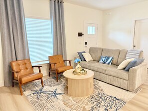 A living room with a beige sofa, two brown leather chairs, a round wooden coffee table, and a star-patterned rug. - Azure & Anchor Coastal Escape W Huge Fenced Yard & Fire Pit + Small-Pet-Friendly (St. Augustine)