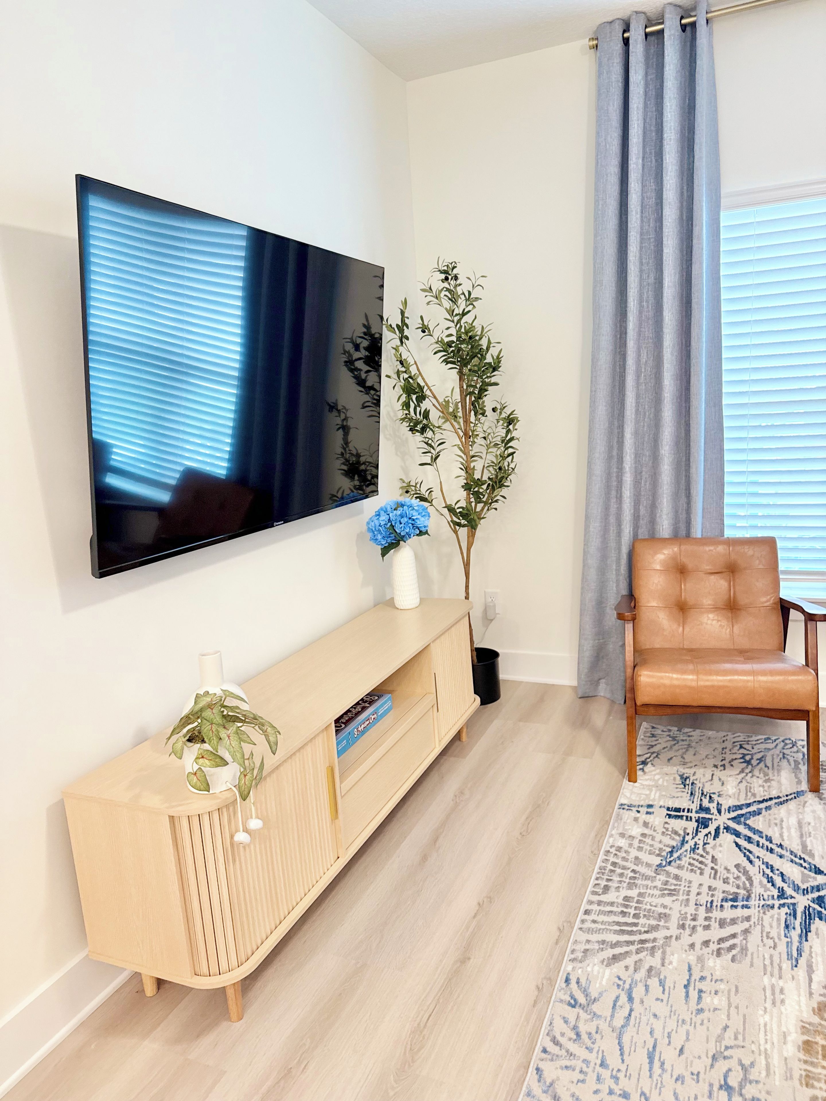 Un salon moderne avec un téléviseur à écran plat fixé au mur, une console en bois agrémentée d’objets décoratifs, un fauteuil en cuir et un tapis à motifs.